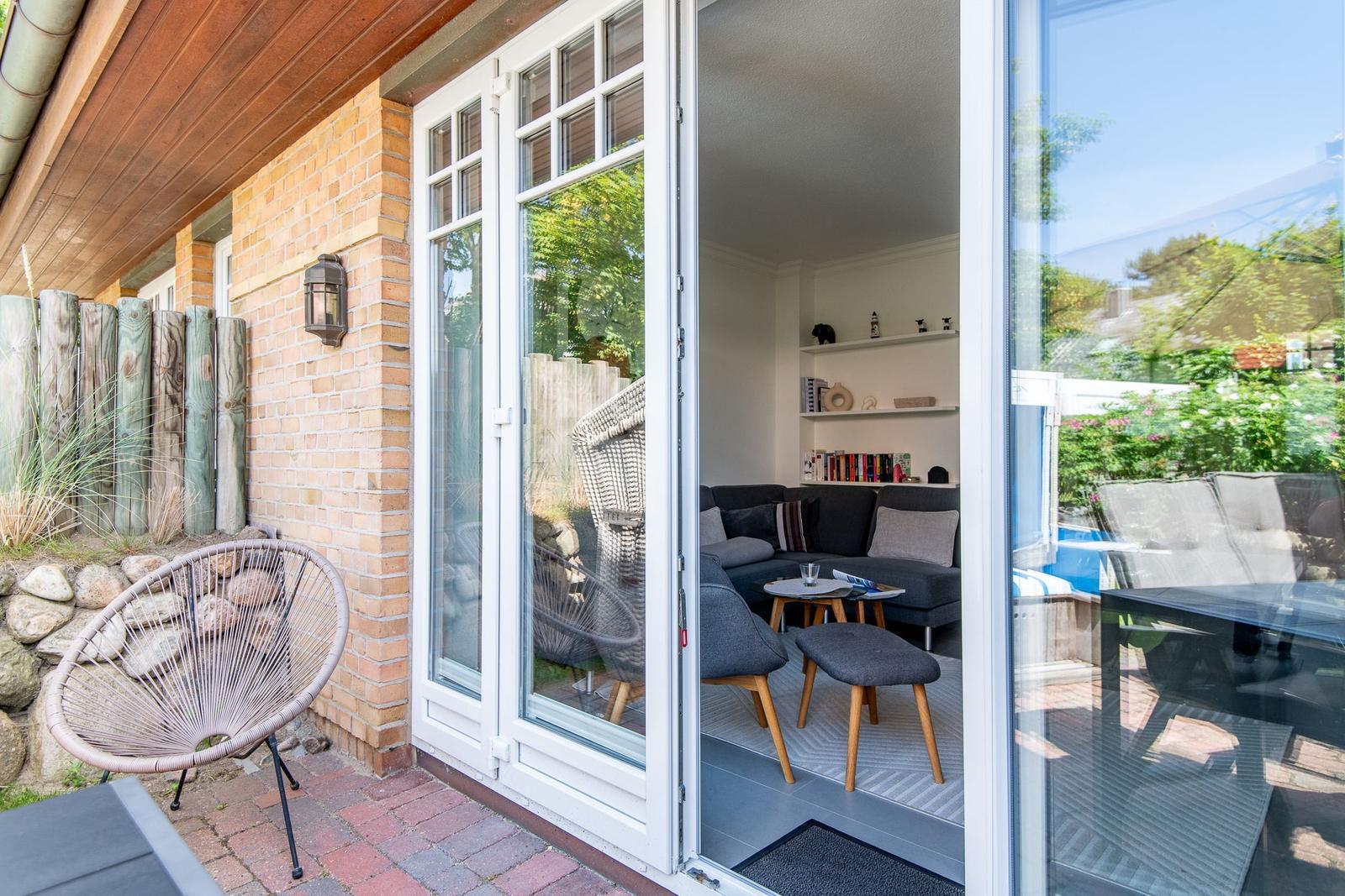 Terrasse mit Sitzgelegenheit und Blick ins Wohnzimmer mit Sofa und Regal.