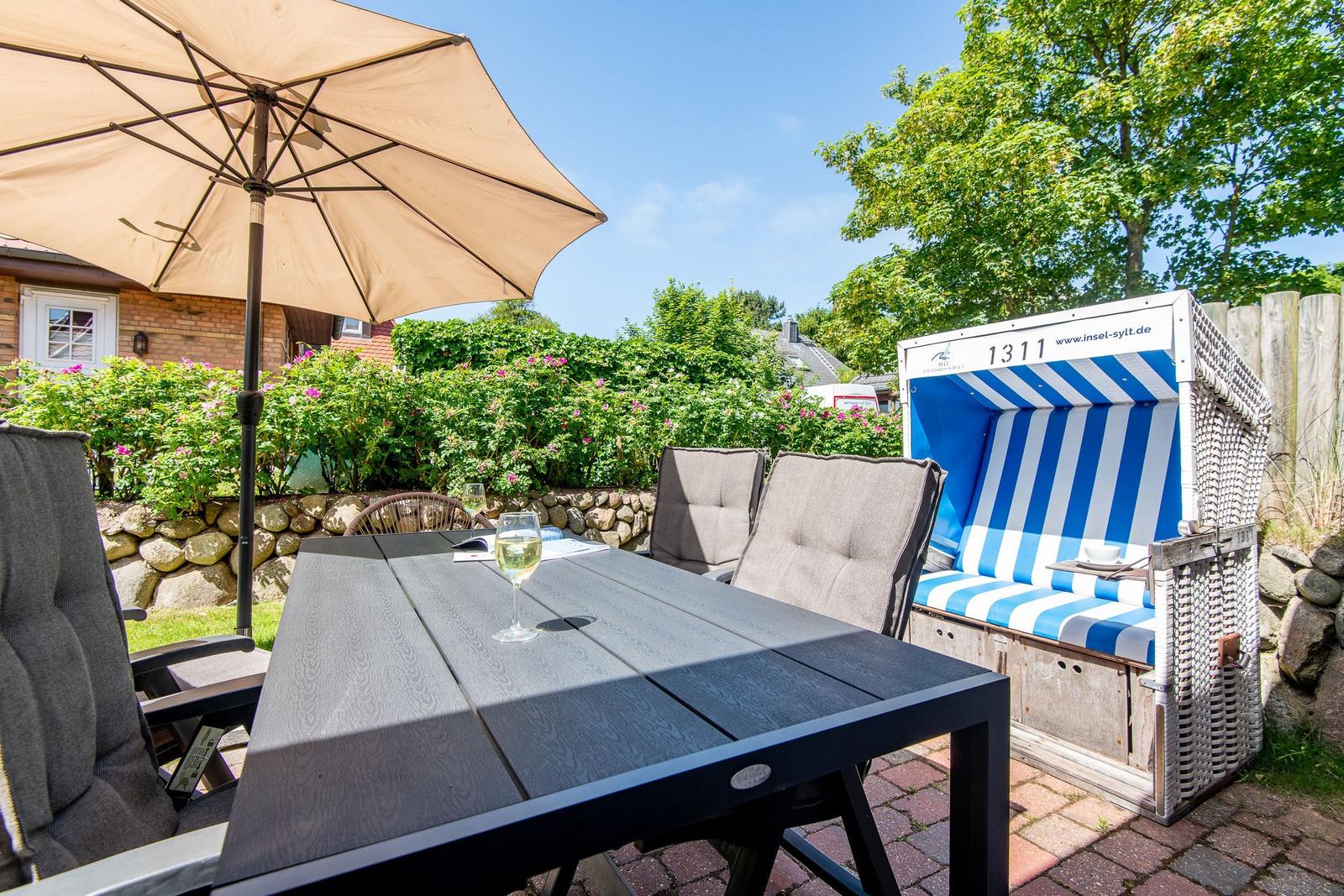 Terrasse mit Tisch, Stühlen und Sonnenschirm. Strandkorb mit blau-weißem Streifenmuster.