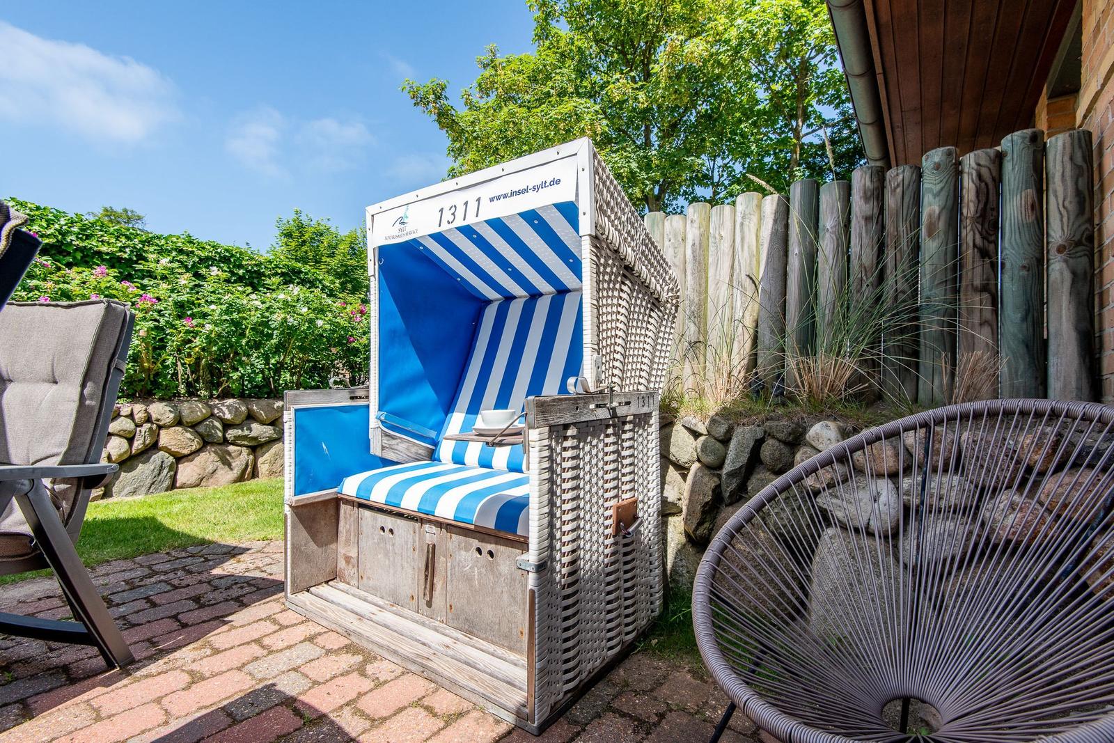 Blauer Strandkorb mit Streifen sitzt auf Steinmauer und Pflanzen im Garten.
