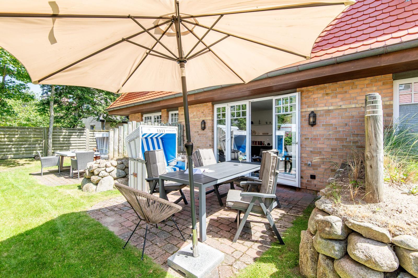 Terrasse mit Tisch, Stühlen und Sonnenschirm neben einem Haus mit Backsteinmauer.