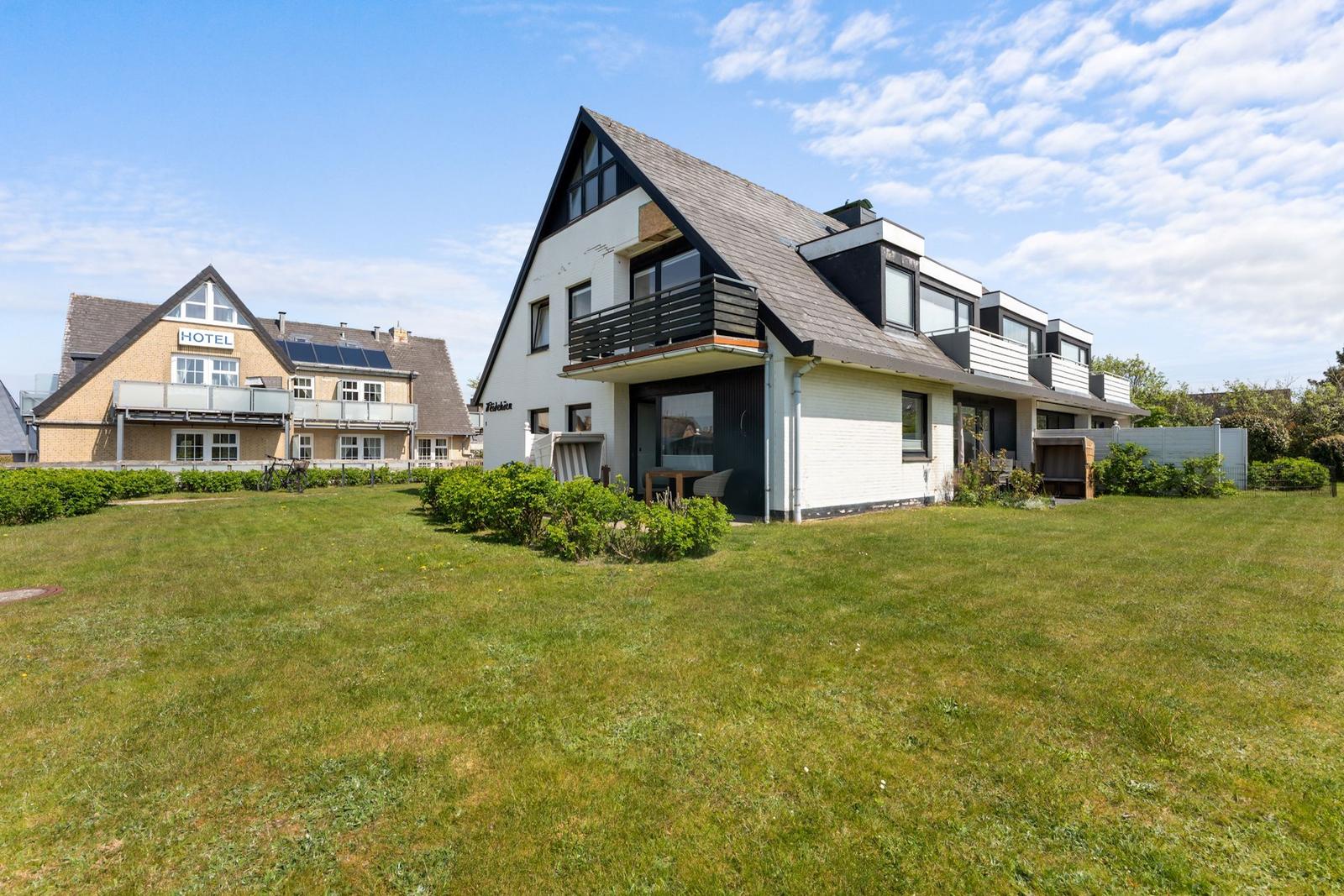 Moderne Villa mit Balkon und Garten. Im Hintergrund ein Hotel mit Solaranlage.
