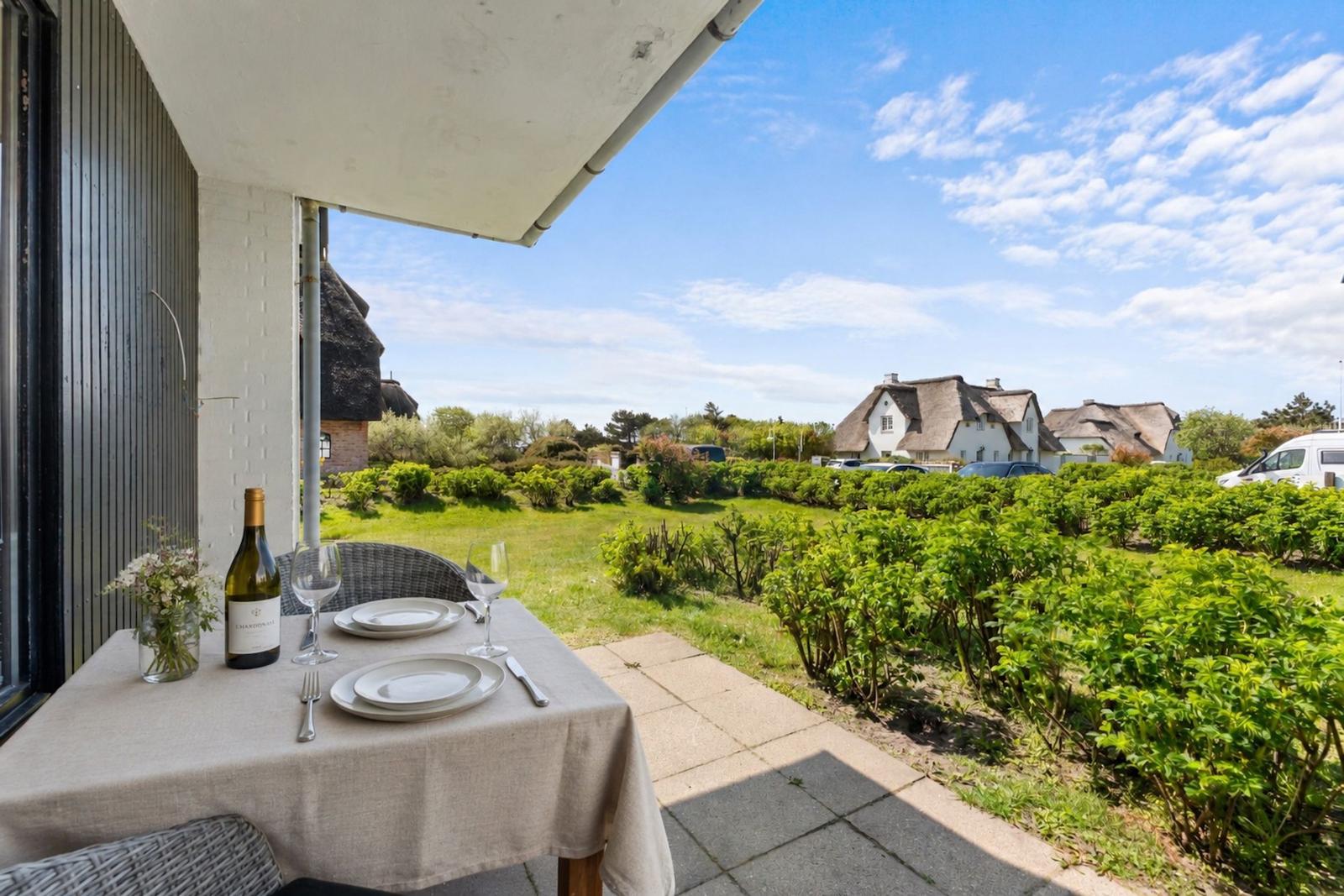 Terrasse mit gedecktem Tisch, Blick auf grüne Gärten und Häuser mit Strohdächern.