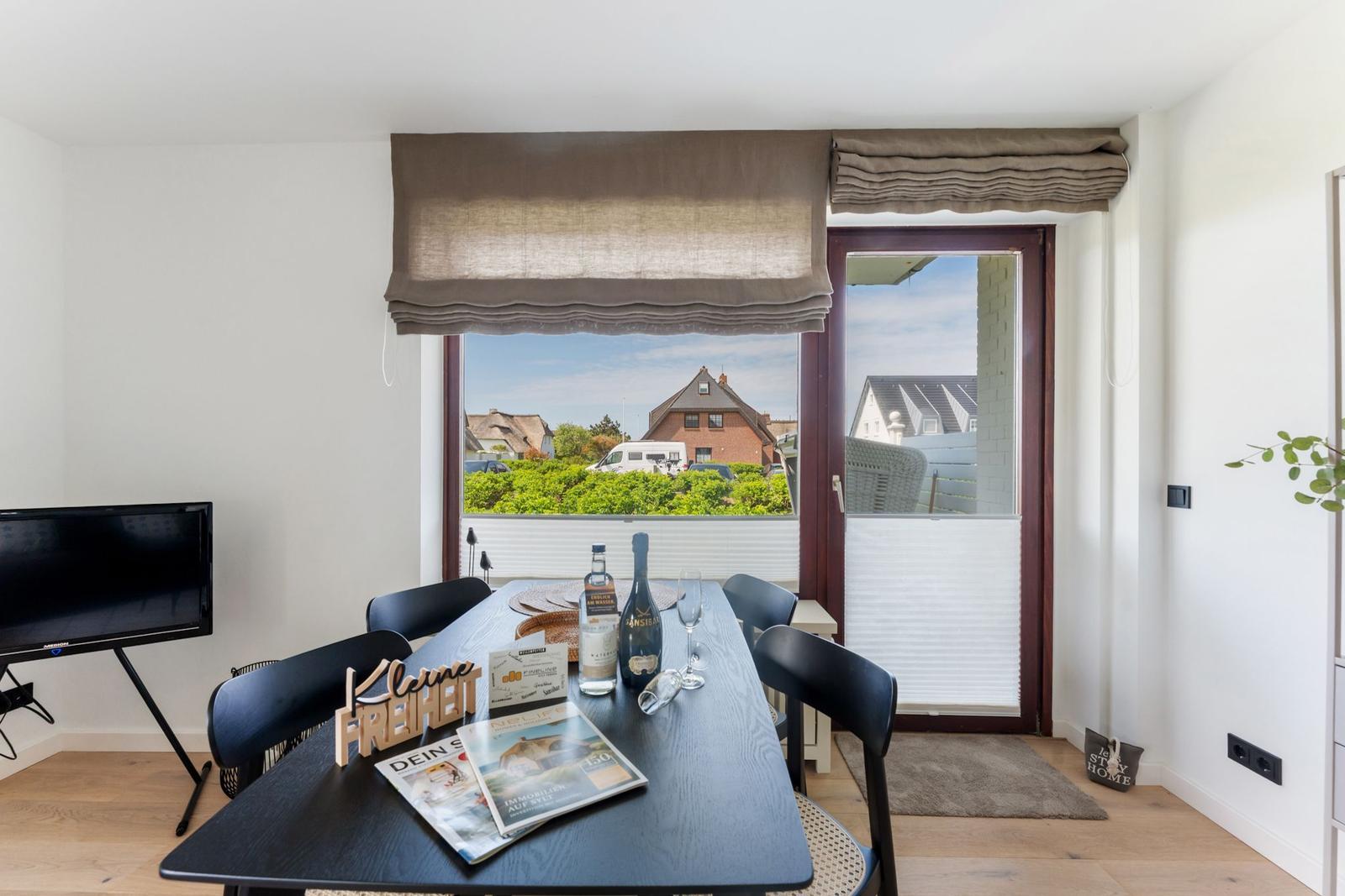 Esszimmer mit Tisch, Stühlen und Blick auf Garten und Häuser.