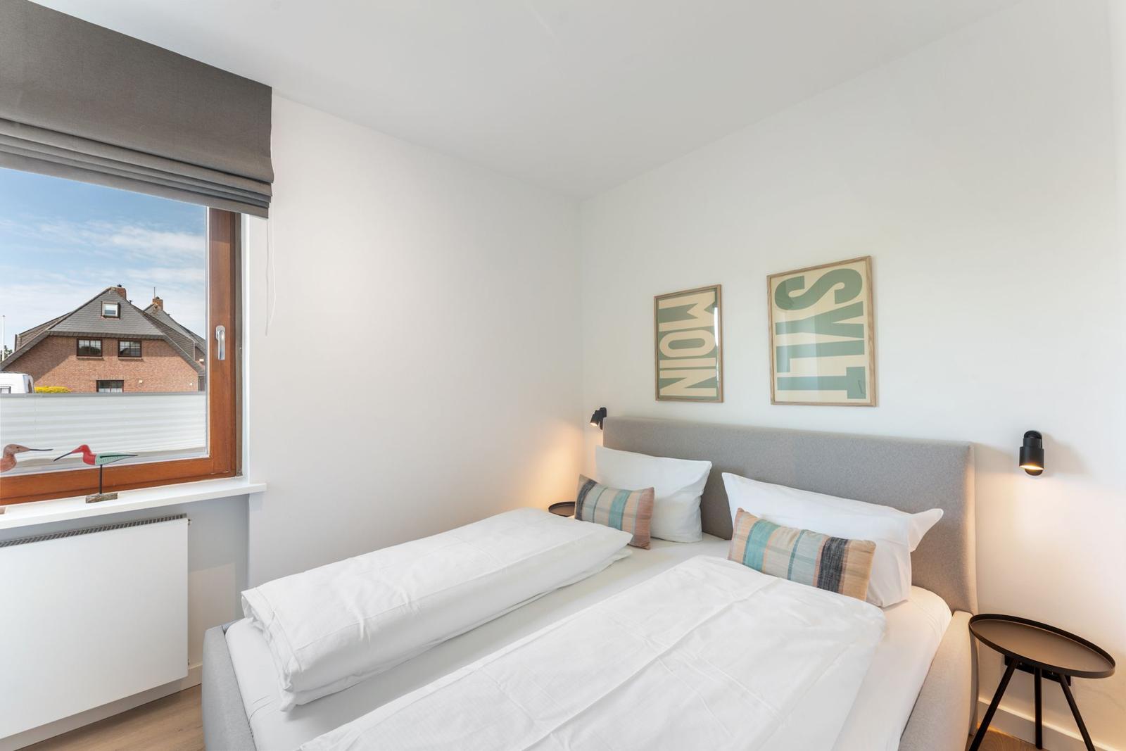 Schlafzimmer mit Bett, Fenster und Wandbildern.