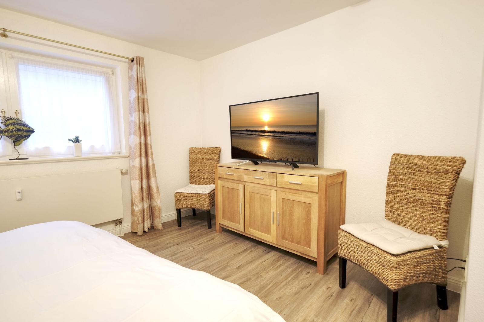 Schlafzimmer mit Bett, Fernseher auf Holzschrank und zwei Stühlen.