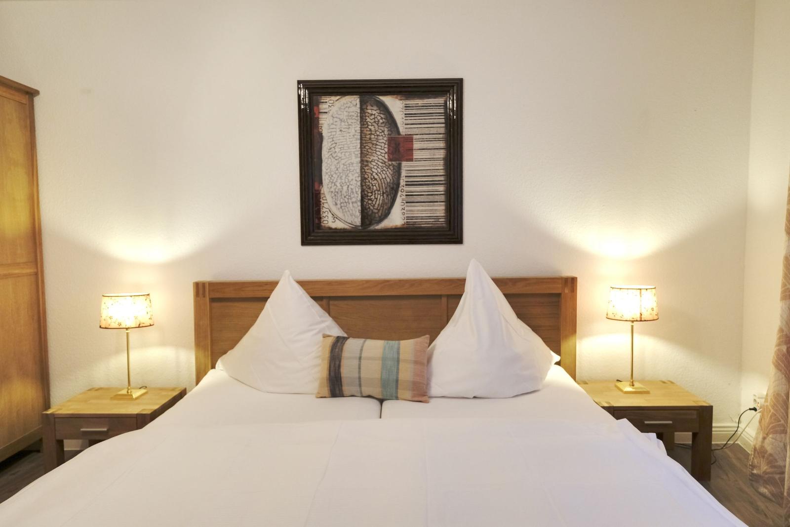 Schlafzimmer mit Bett, Nachttischen und Lampen. An der Wand hängt ein Bild.