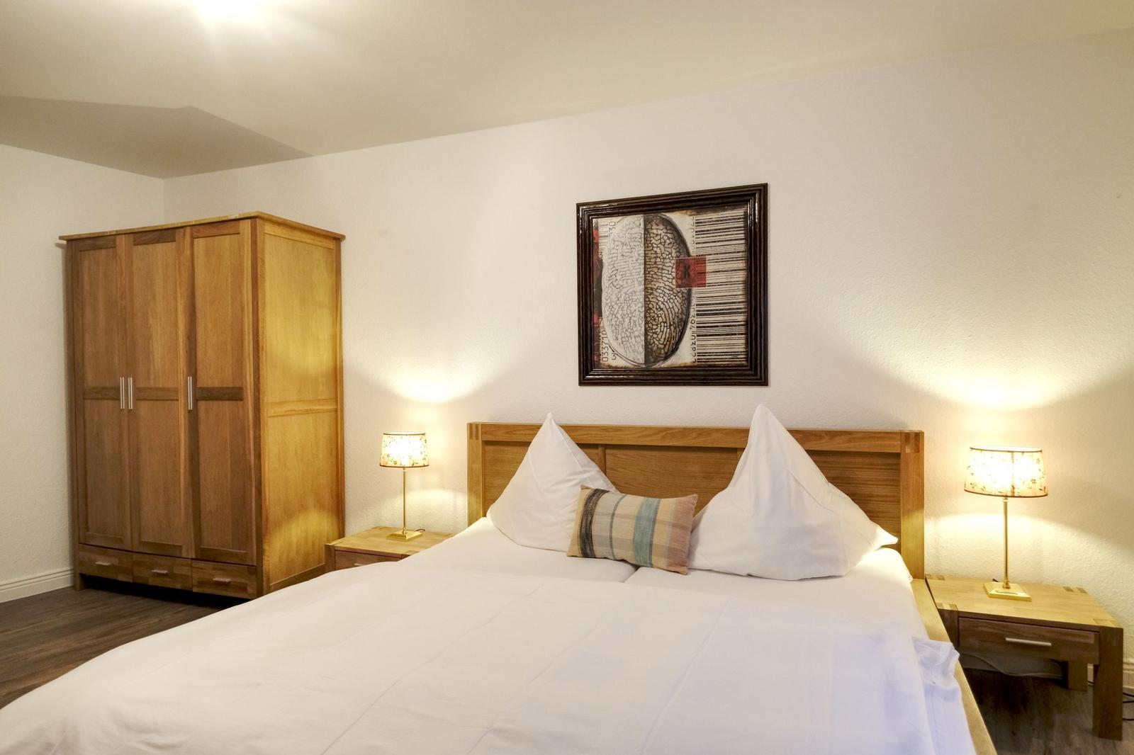 Schlafzimmer mit Bett, Nachttischen und Kleiderschrank. Wandbild über dem Bett.