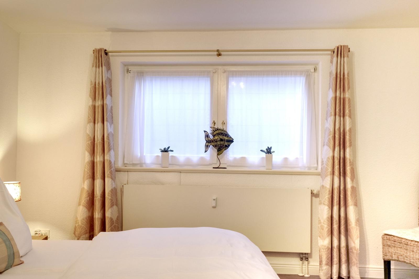Ein Schlafzimmer mit Bett, Fenster, Vorhängen und einer Fischdekoration auf dem Fensterbrett.
