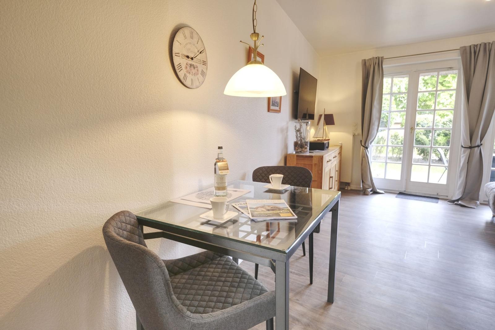 Esszimmer mit Glas-Tisch, Stühlen und Wanduhr. Durchgang zur Terrasse mit Fenstertür.