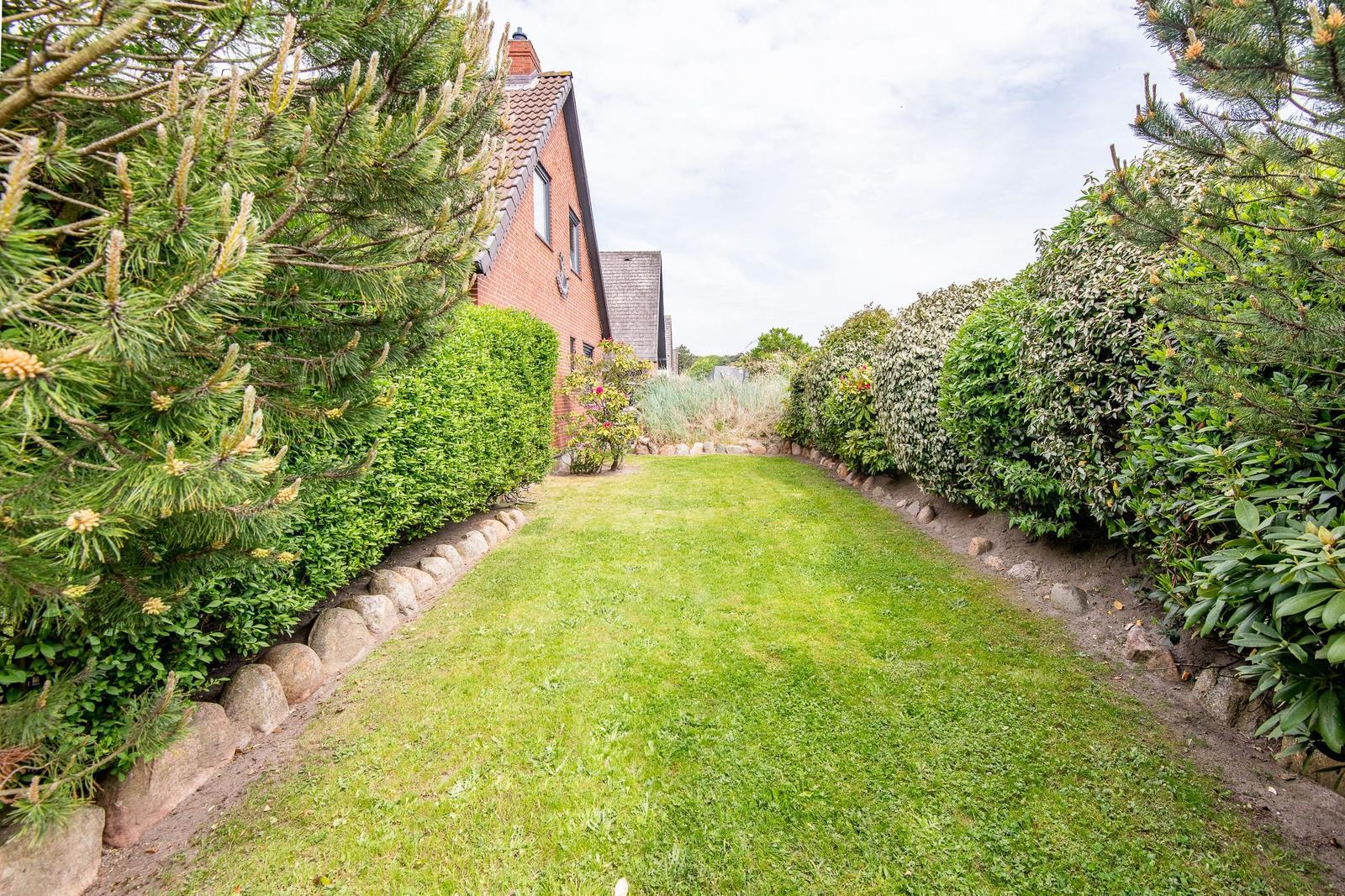 Garten mit Rasenfläche, Beete und Hecken entlang eines Hauses.
