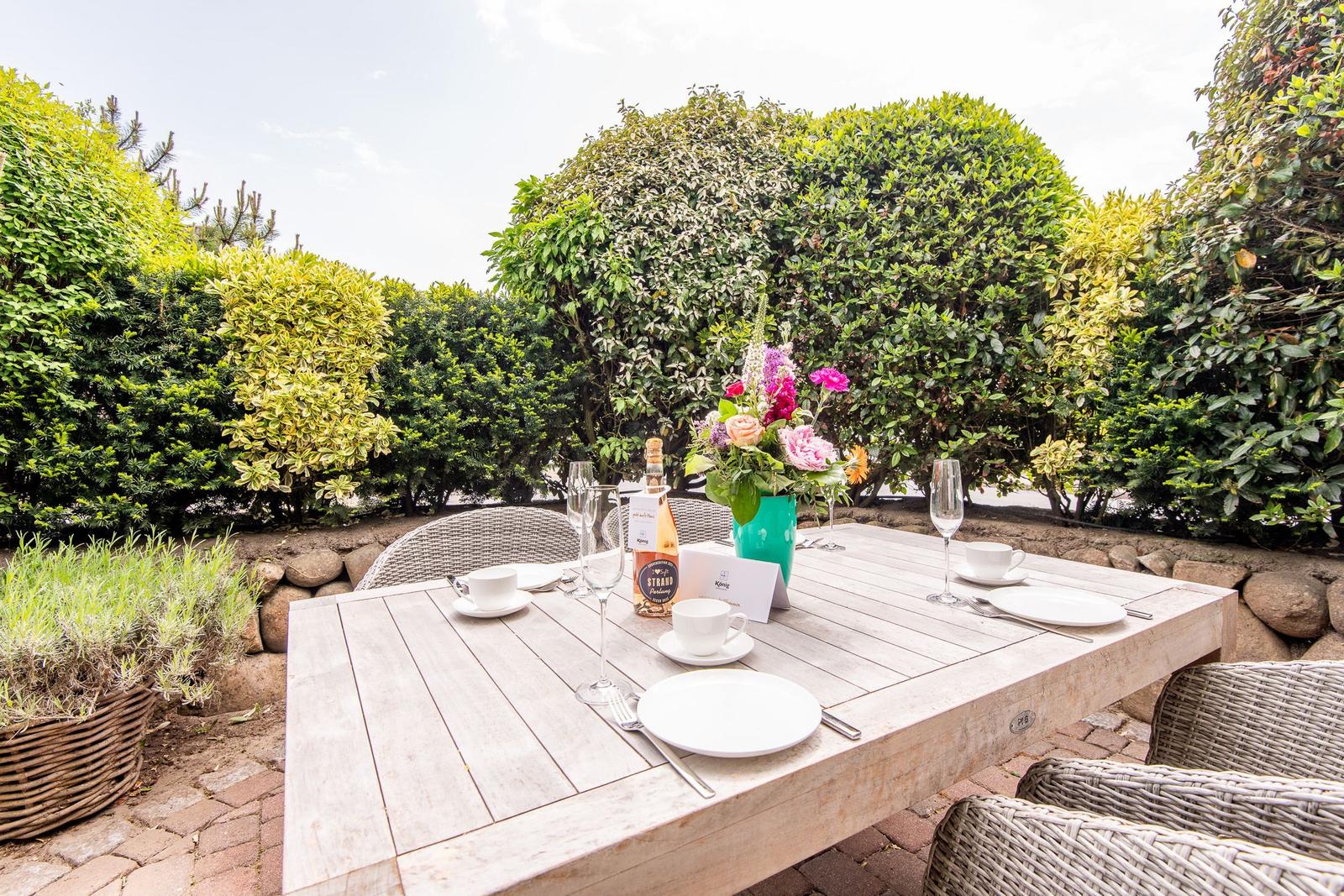 Garten-Tisch mit Platz für vier Personen, Blumen und Weinflasche.