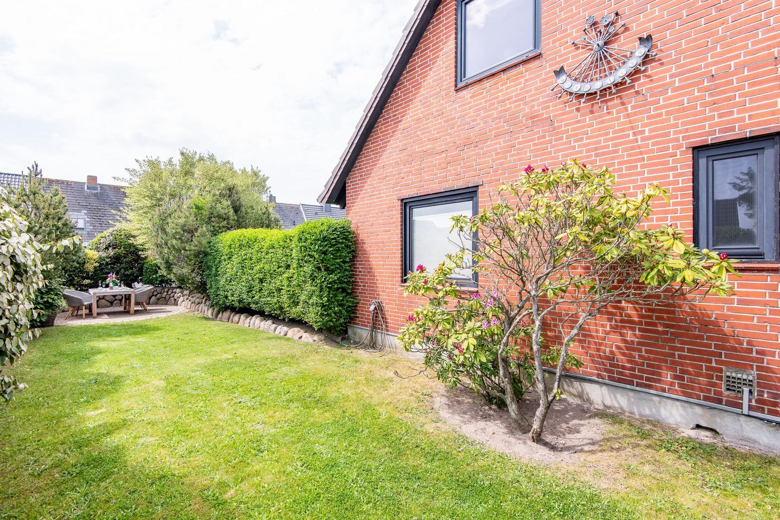 Roter Backsteinbau mit Garten, Tisch und Stühlen, Blumensträucher und Hecke.
