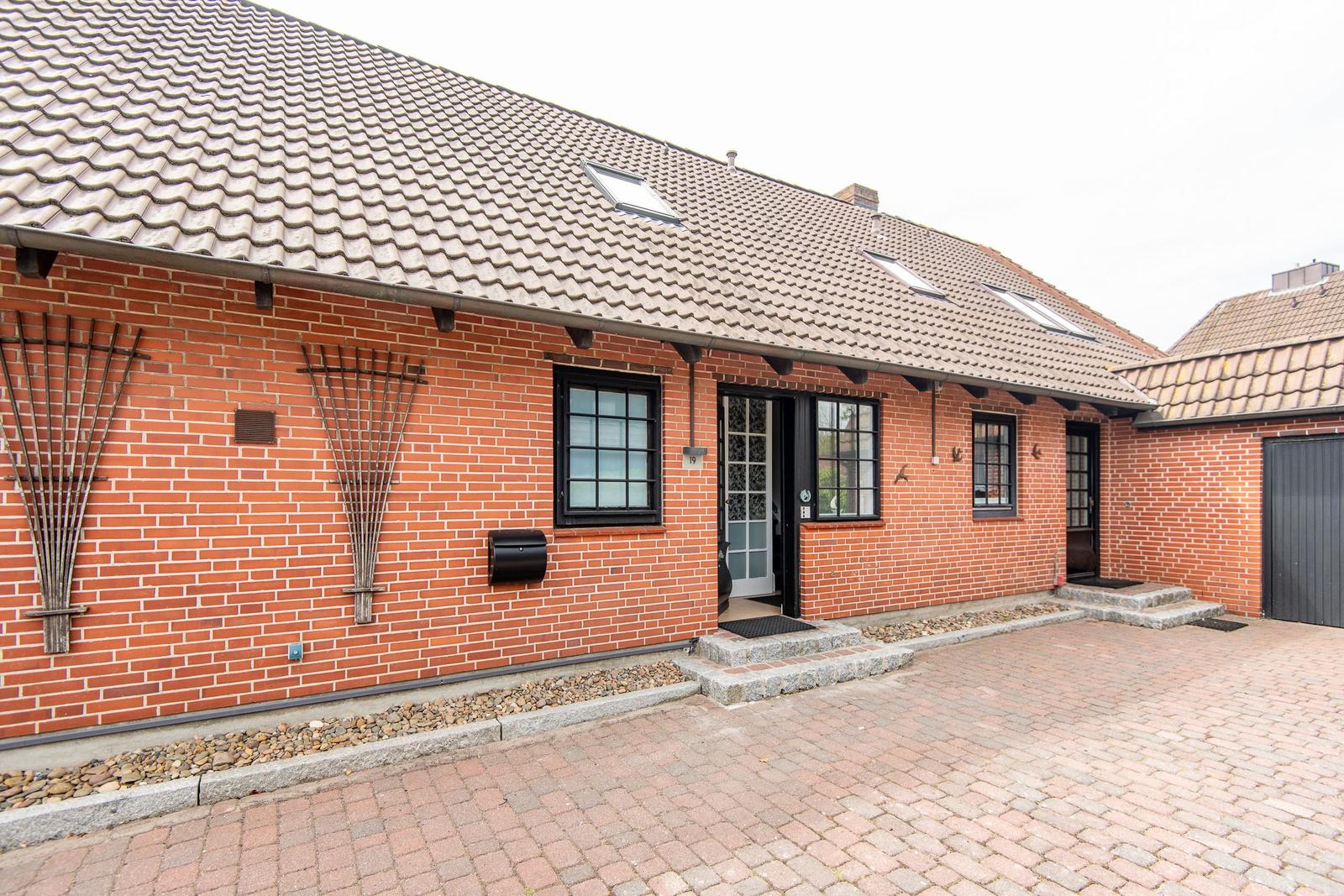 Rotes Backsteingebäude mit Dachfenstern und Eingangstür. Pflasterweg und Steinplatten.
