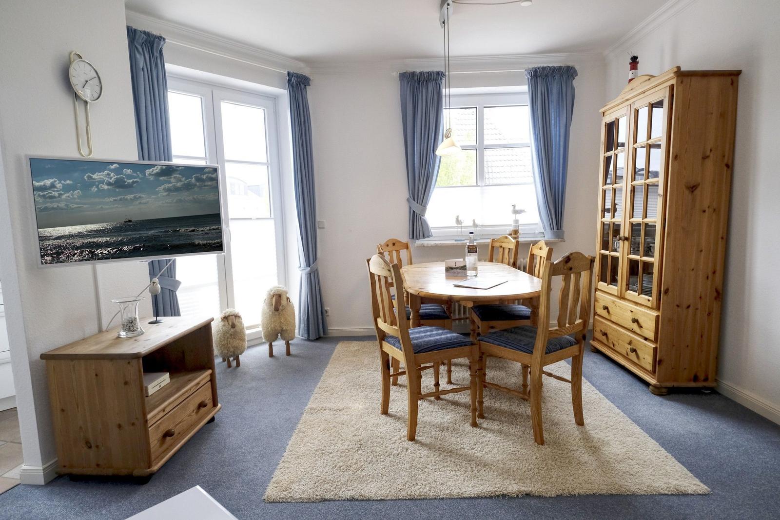 Dining room with wooden table, chairs, and cabinet. TV, curtains, and rug visible.
