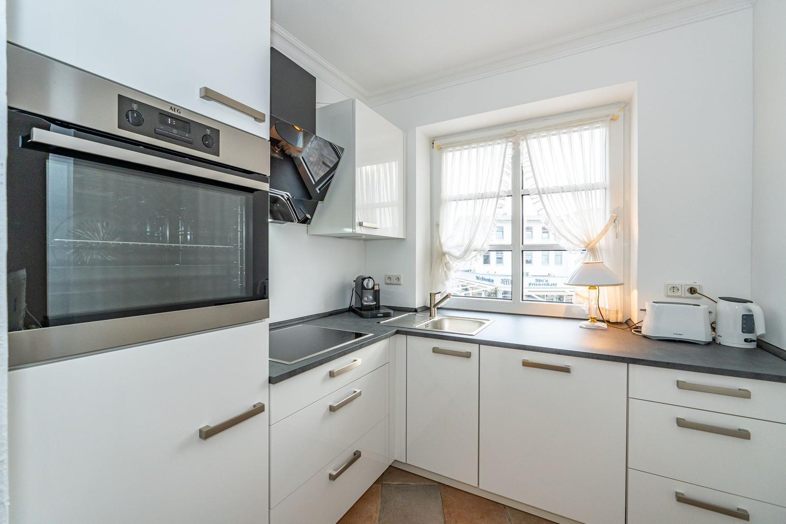 Kitchen with white cabinets, stainless steel oven, and window with curtains.