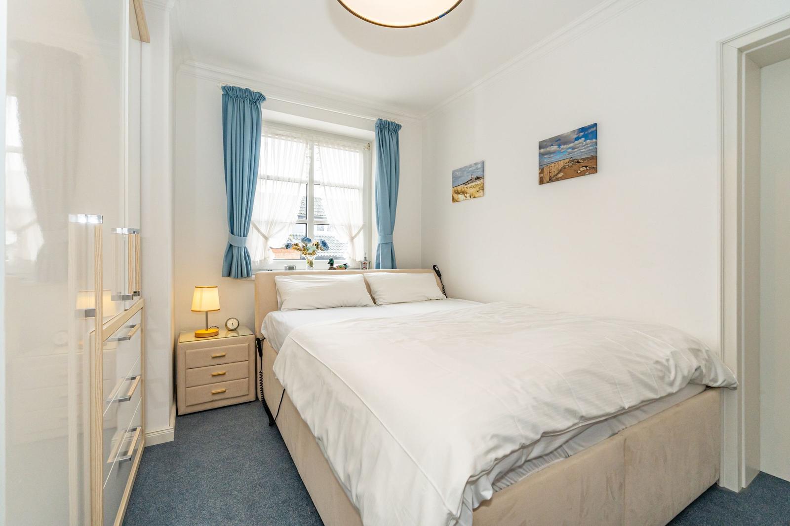 Bedroom with bed, nightstand, and window with blue curtains.
