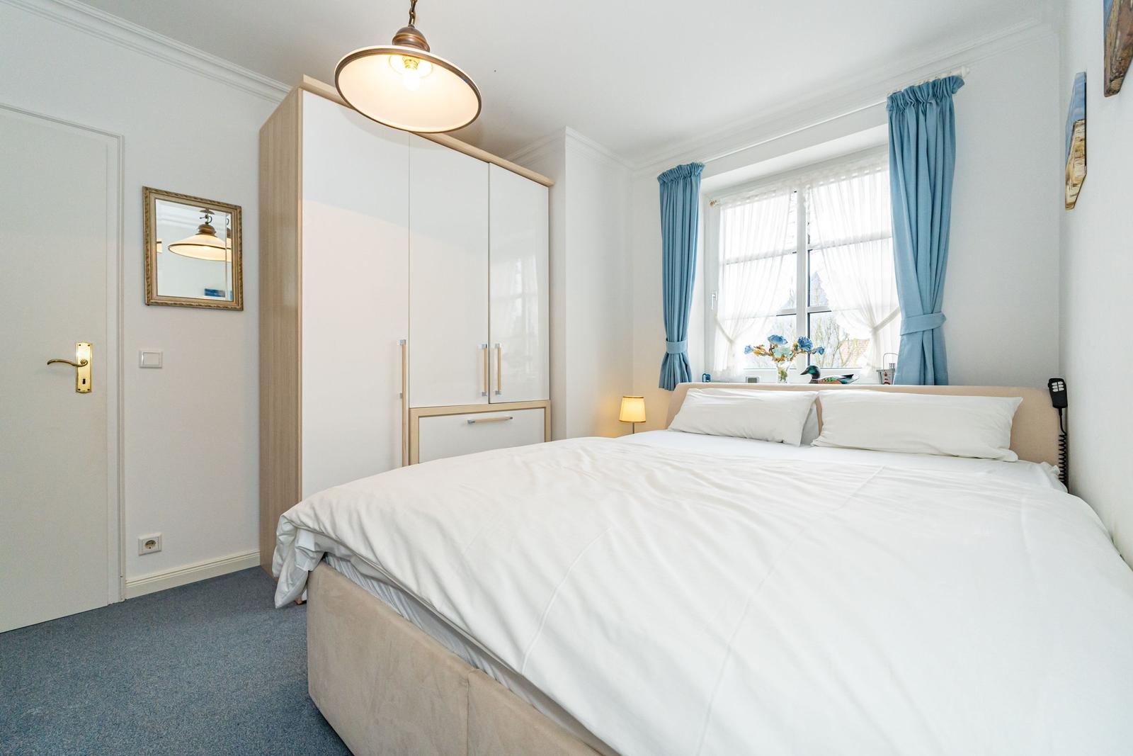 Bedroom with bed, wardrobe, and window with blue curtains.