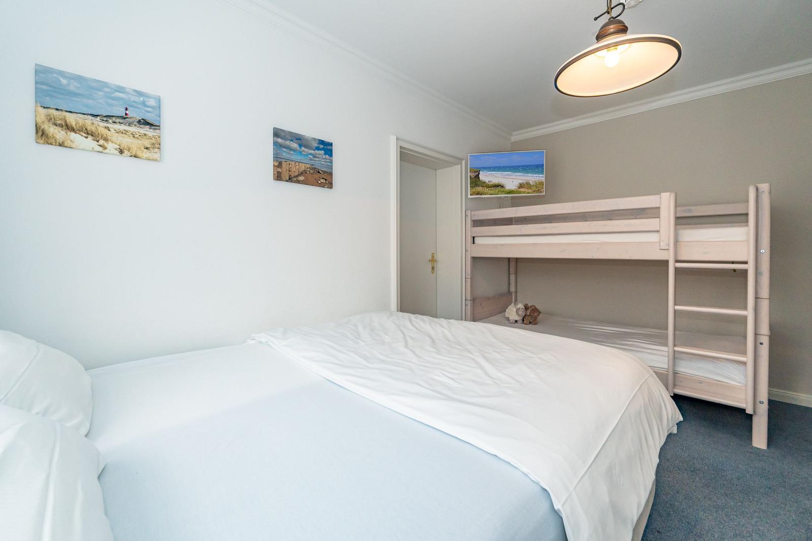 Bedroom with double bed and two-tiered mattress, next to a bunk bed with wooden frame.