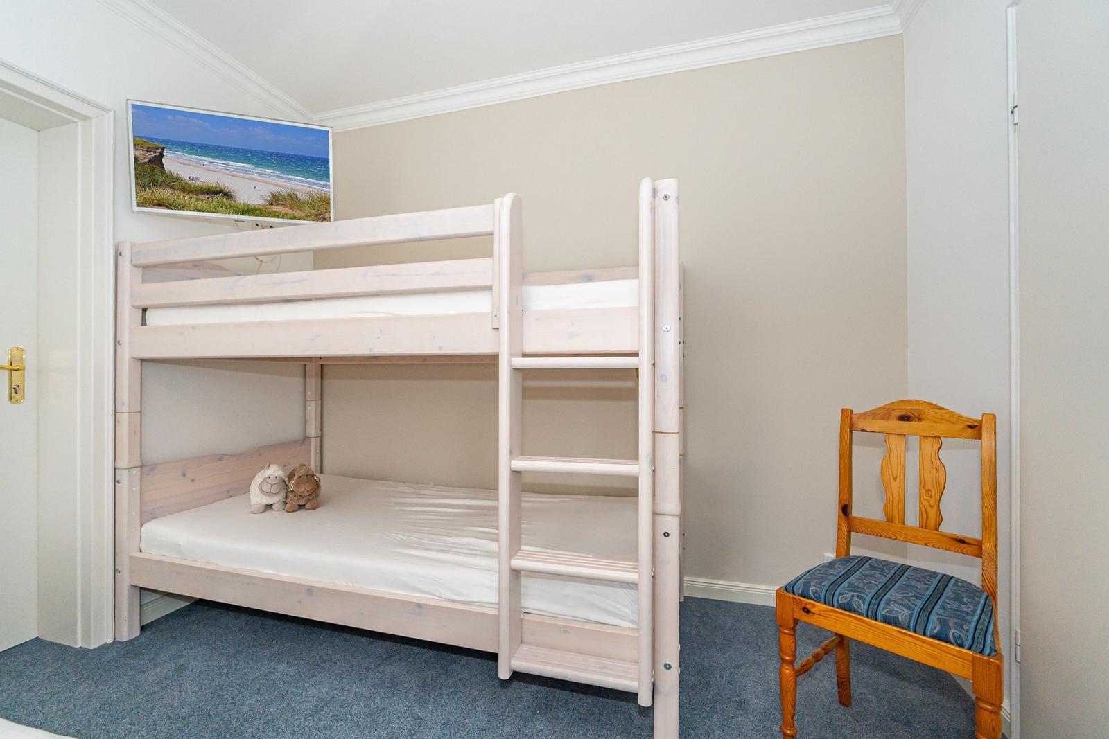 A bedroom with bunk bed, chair, and wall picture