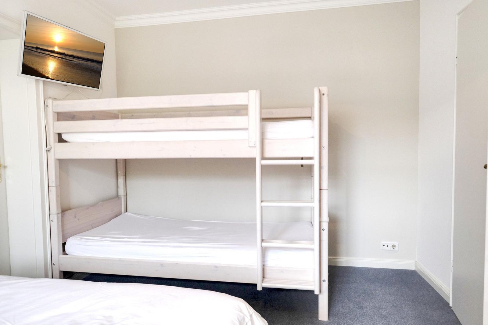 Room with bunk bed, TV, and gray carpet flooring.