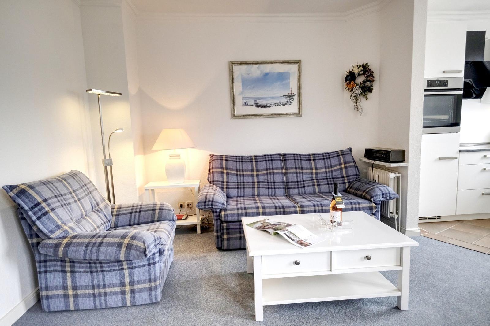 Living room with sofa and armchair, white coffee table, and kitchen area.