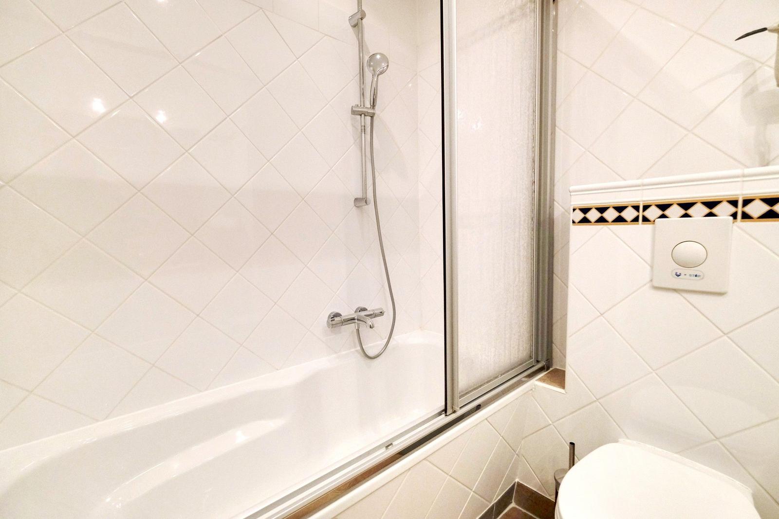 Bath with shower, toilet, and tiled wall with mosaic strip.