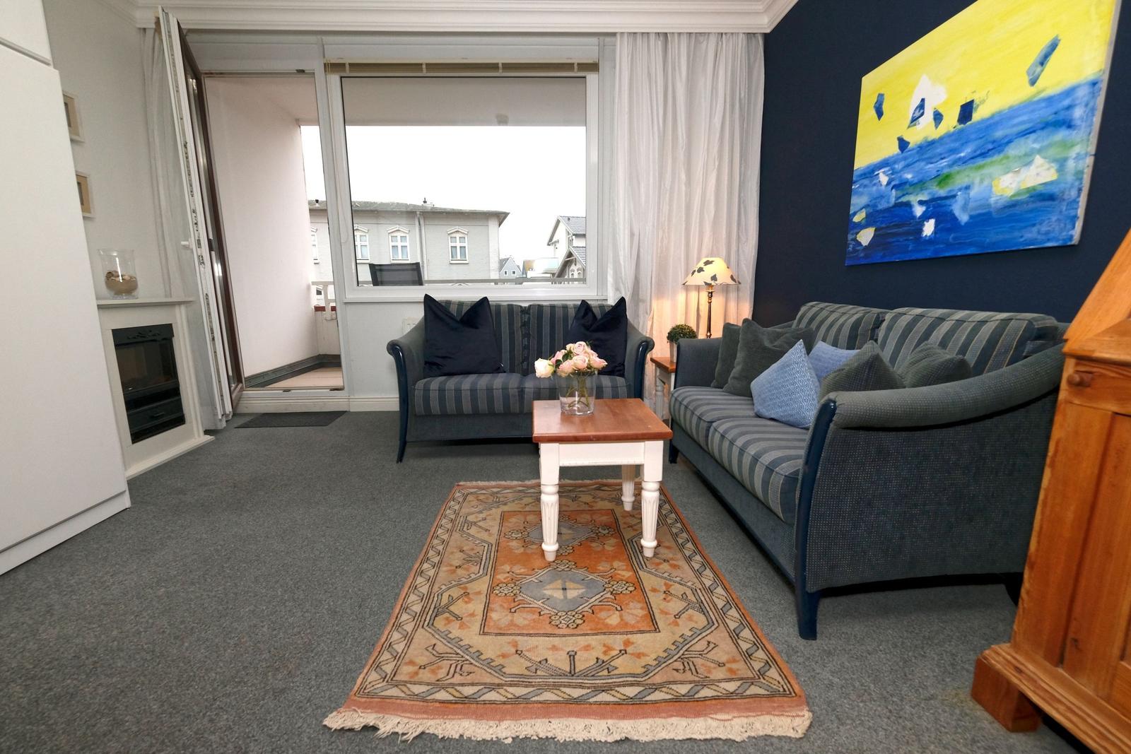Wohnzimmer mit Sofa, Couchtisch und Teppich. Fenster und Balkon sind sichtbar.