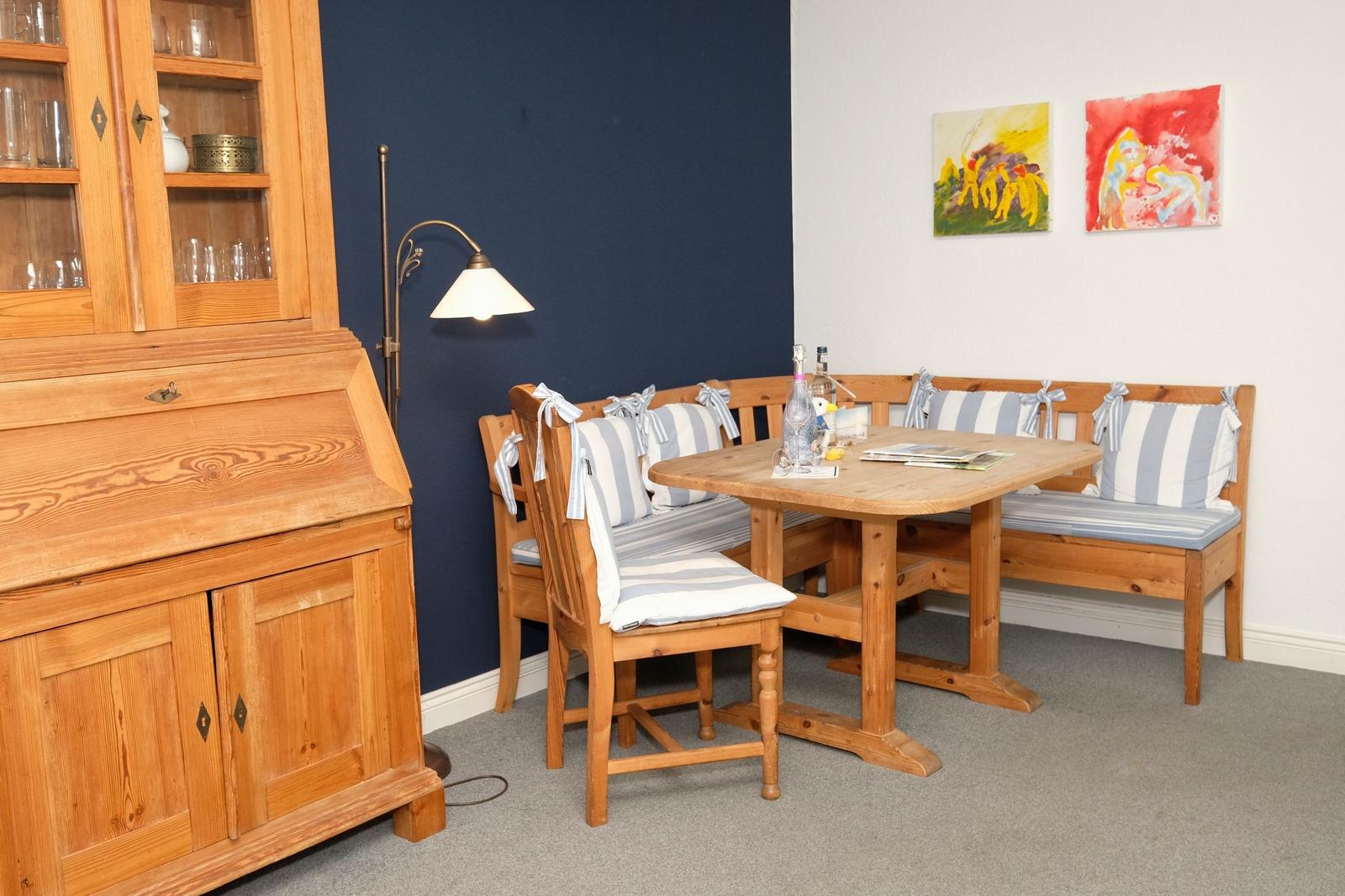 Esszimmer mit Holztisch, Bänken und Stühlen, Glasvitrine und Wandbildern.