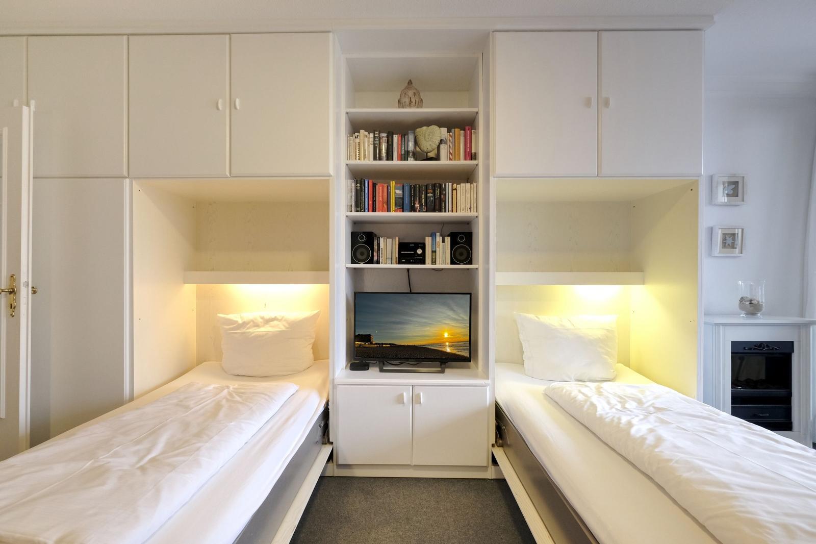 Zwei Einzelbetten mit Nachttischen und integriertem TV-Bereich mit Bücherregal.