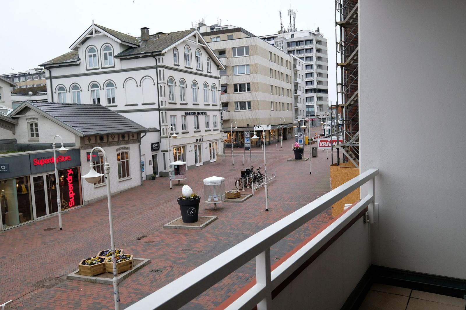 Blick von Balkon auf belebte Straße mit Geschäften und Parkplätzen.