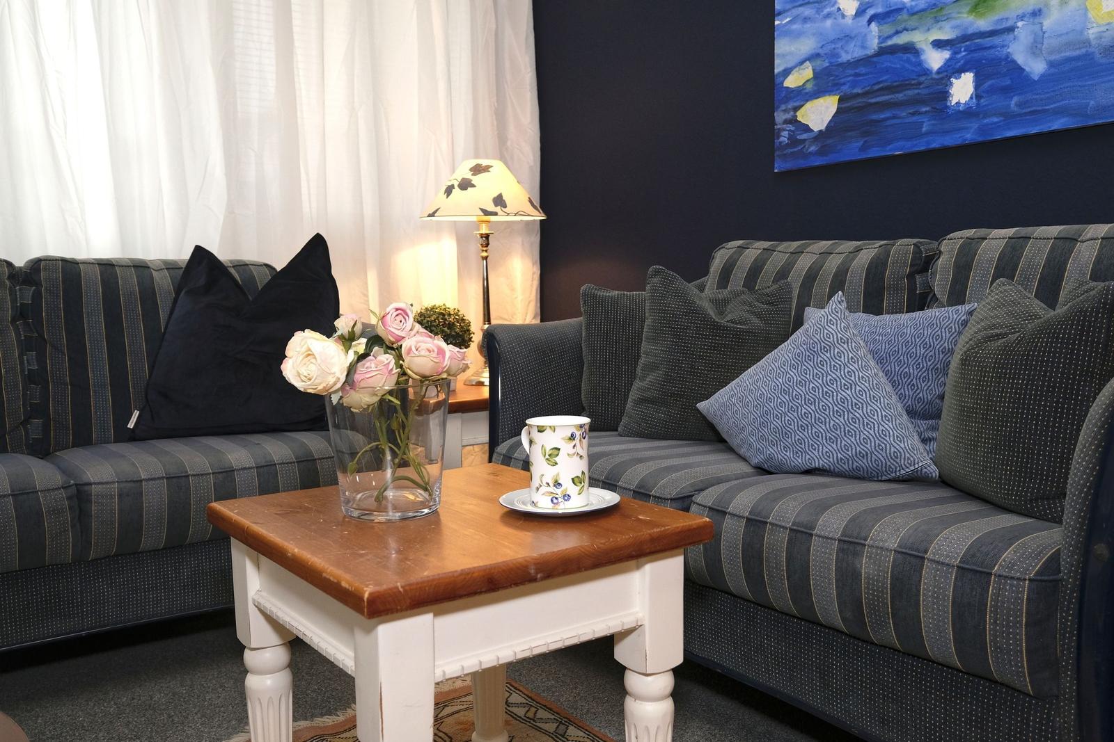 Zwei Sofas mit Kissen, Tisch mit Blumen und Tasse, Wandbild und Lampe.