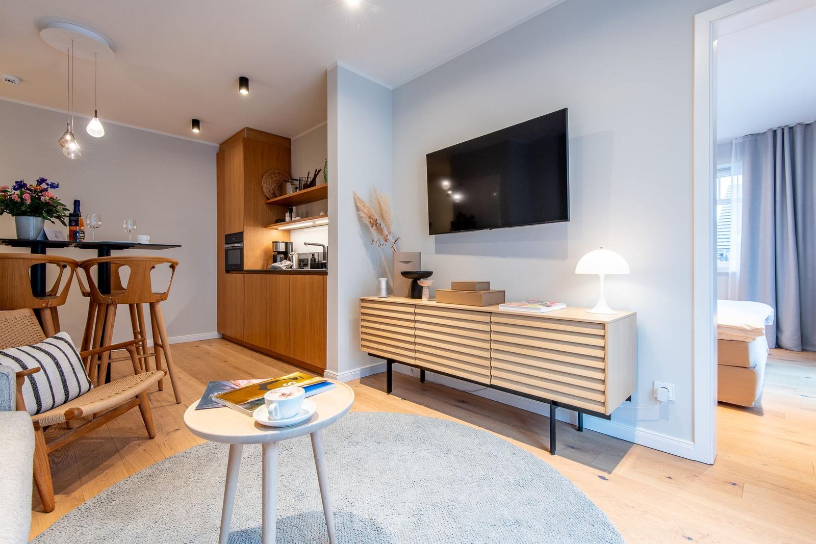 Living area with TV, sideboard, dining table, and kitchenette. Entrance to bedroom.