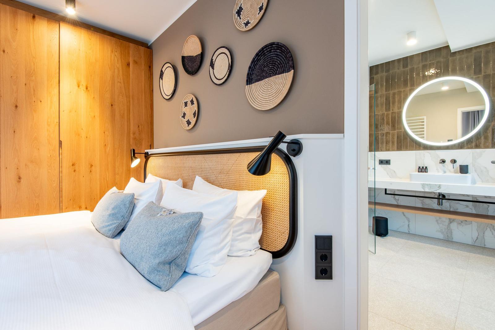 Bedroom with bed, wooden wall, and wall decor. Adjacent room with sink and round mirror.