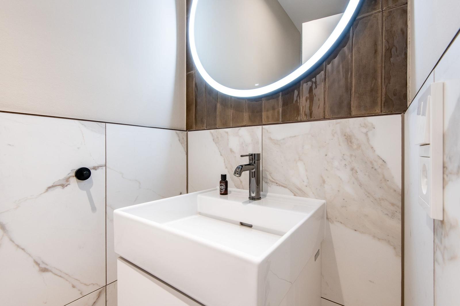Sink with mirror and modern faucet on marble wall.