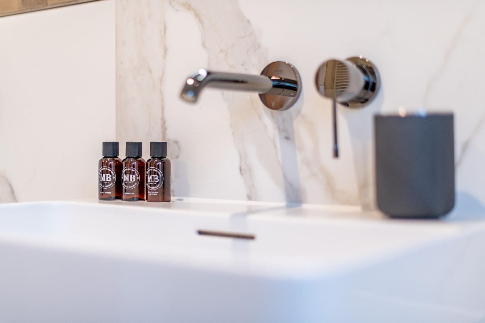 Sink with showerhead and three bottles of care products on marble wall.