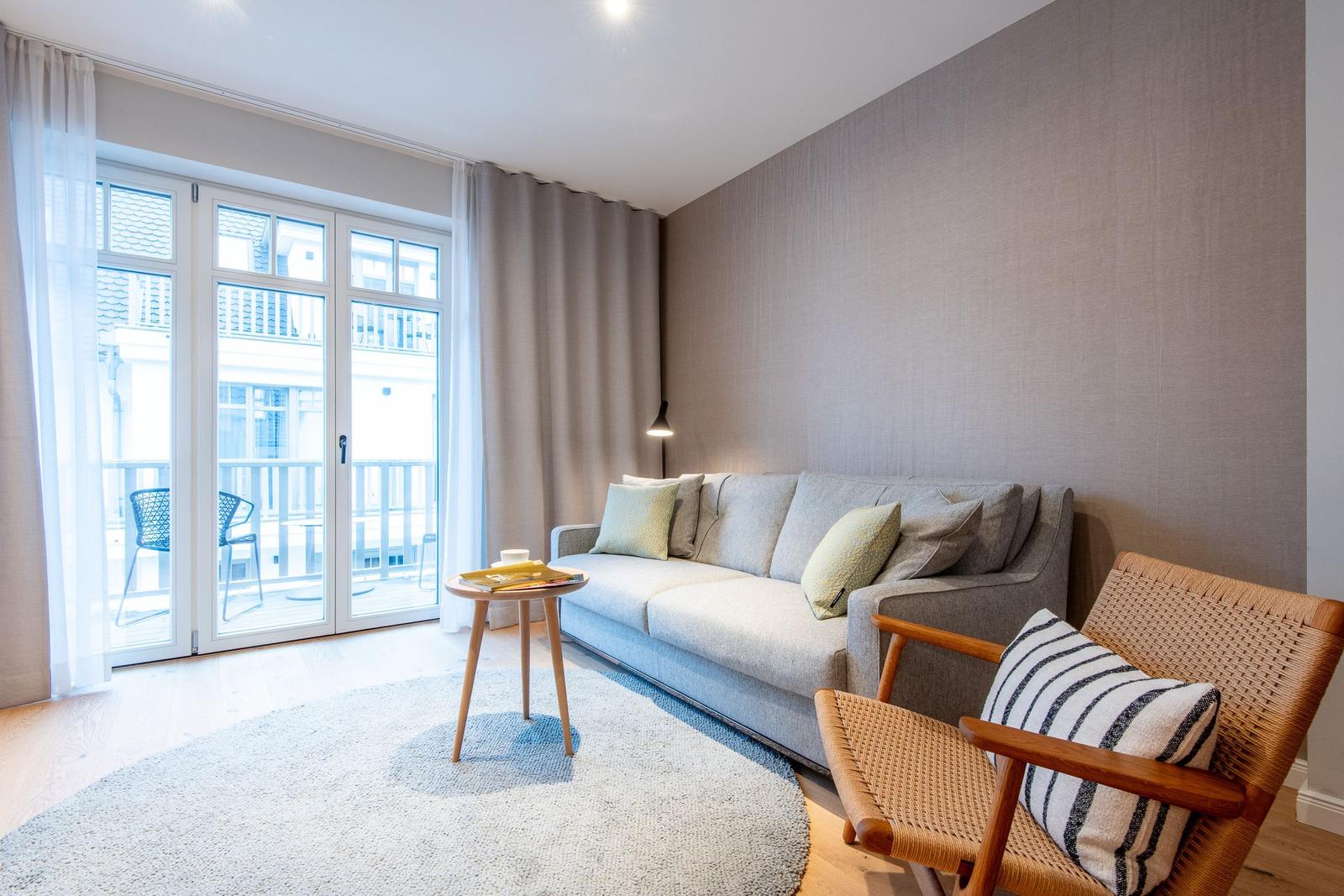 Living room with sofa, chair, and balcony. Wooden floor and round rug.