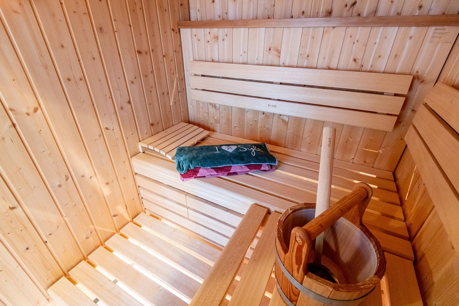 Sauna with wooden bench, towel, and bucket with ladle.