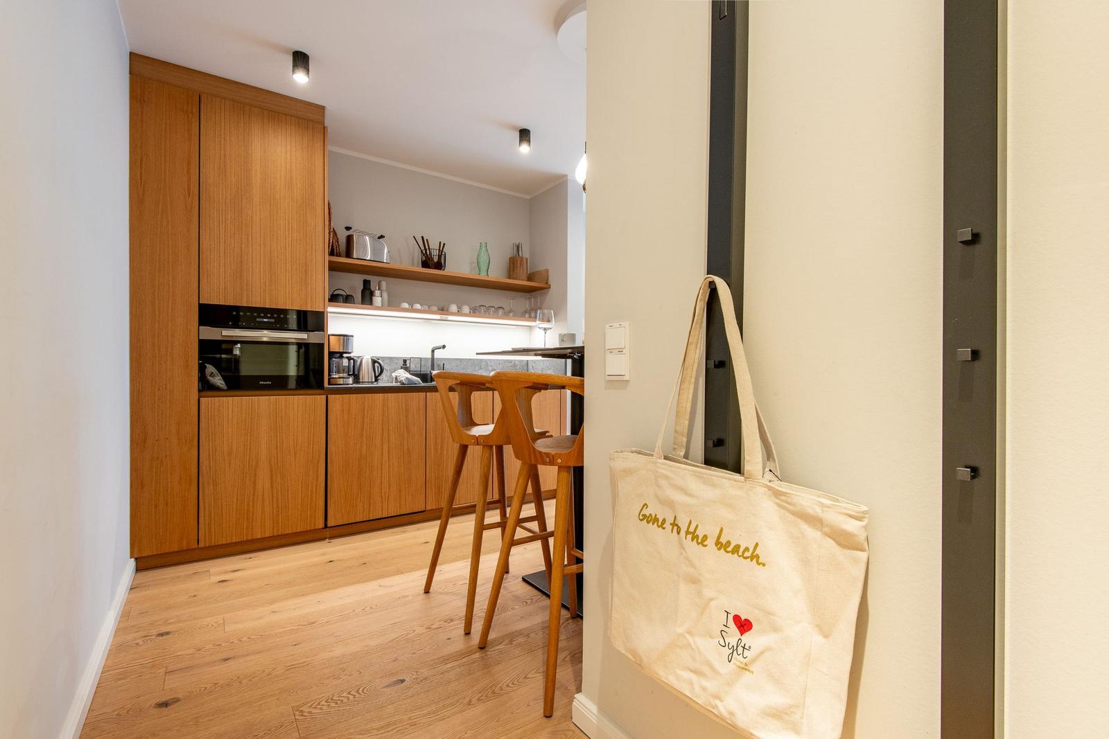 Kitchen with wooden furniture and bar stools. A bag hangs on the wall.