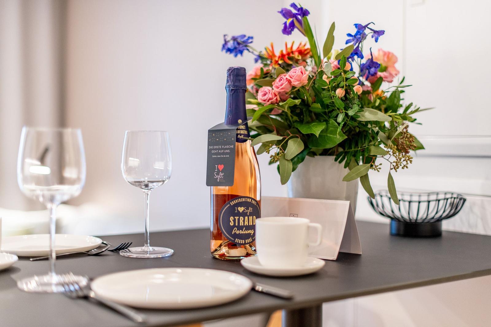 Table with flower vase, bottle of sparkling wine, and dishes.