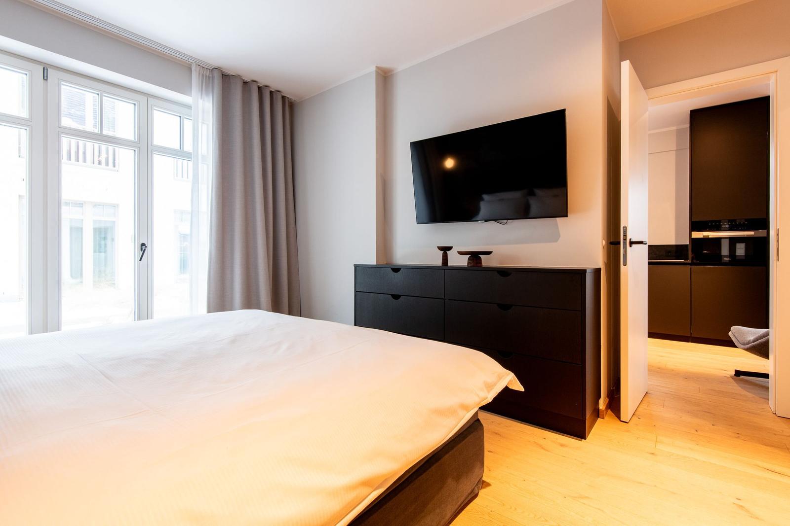 Schlafzimmer mit Bett, TV und Blick auf Balkon.