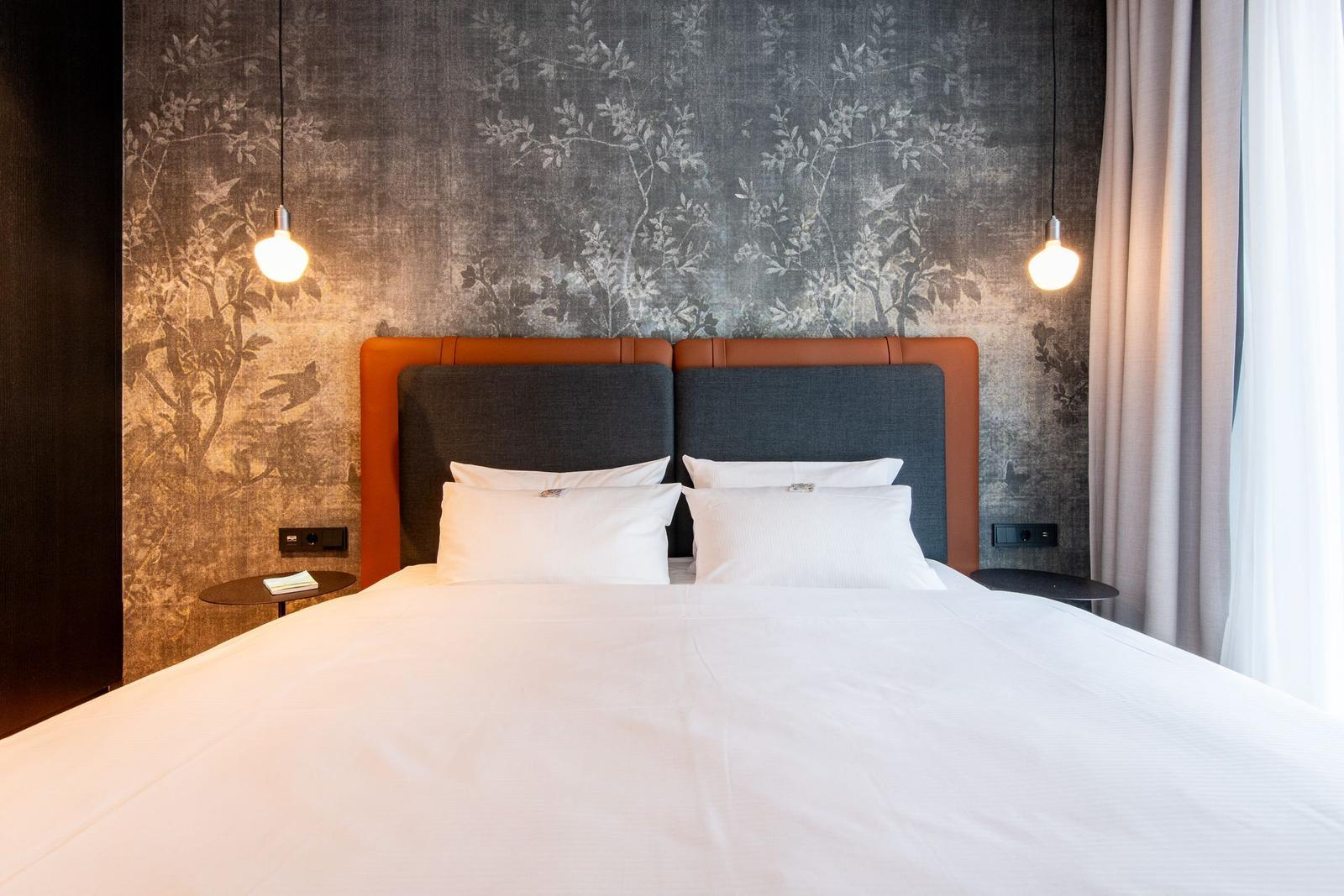 Ein Bett mit weißer Bettwäsche, einem grauen Kopfteil und orangefarbenen Akzenten an der Wand.