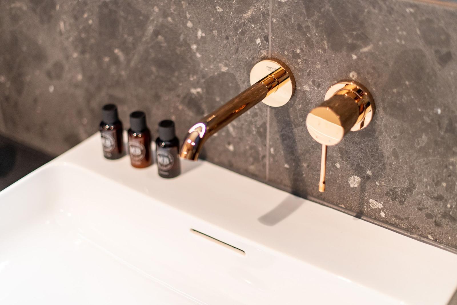 Waschbecken mit goldenem Wasserhahn und drei Fläschchen auf der Oberfläche.