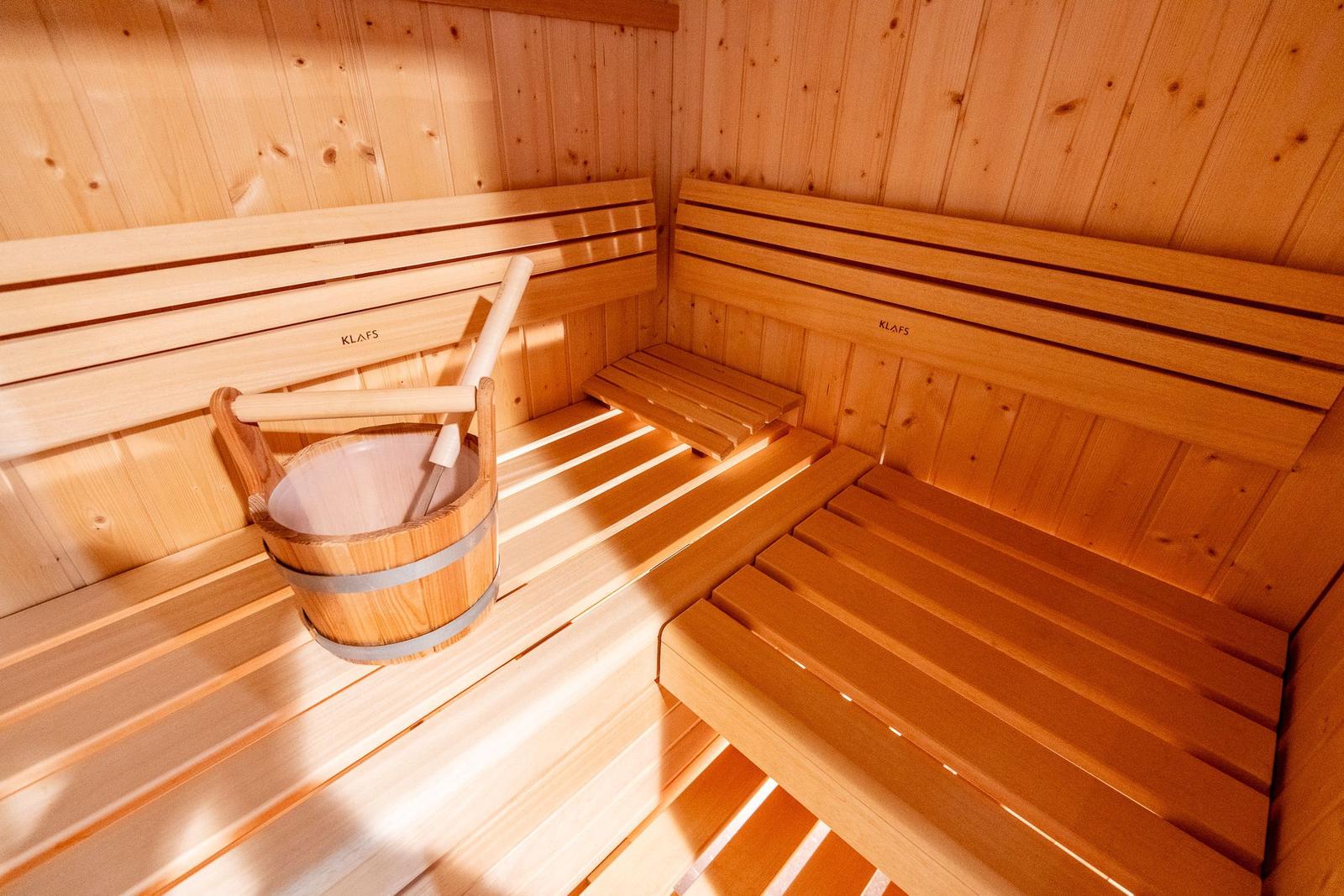 Holzsauna mit Sitzbänken und Eimer. Markenname KLAFS sichtbar.