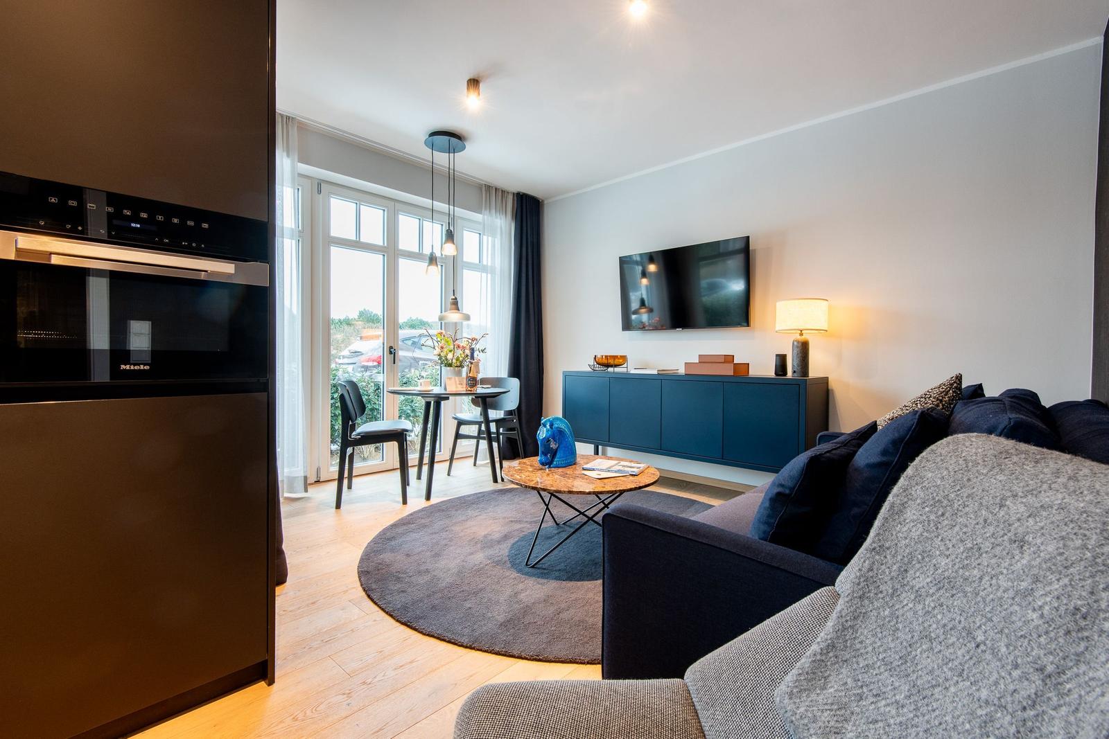 Wohnbereich mit Sofa, Couchtisch, Fernseher und Küchenzeile.