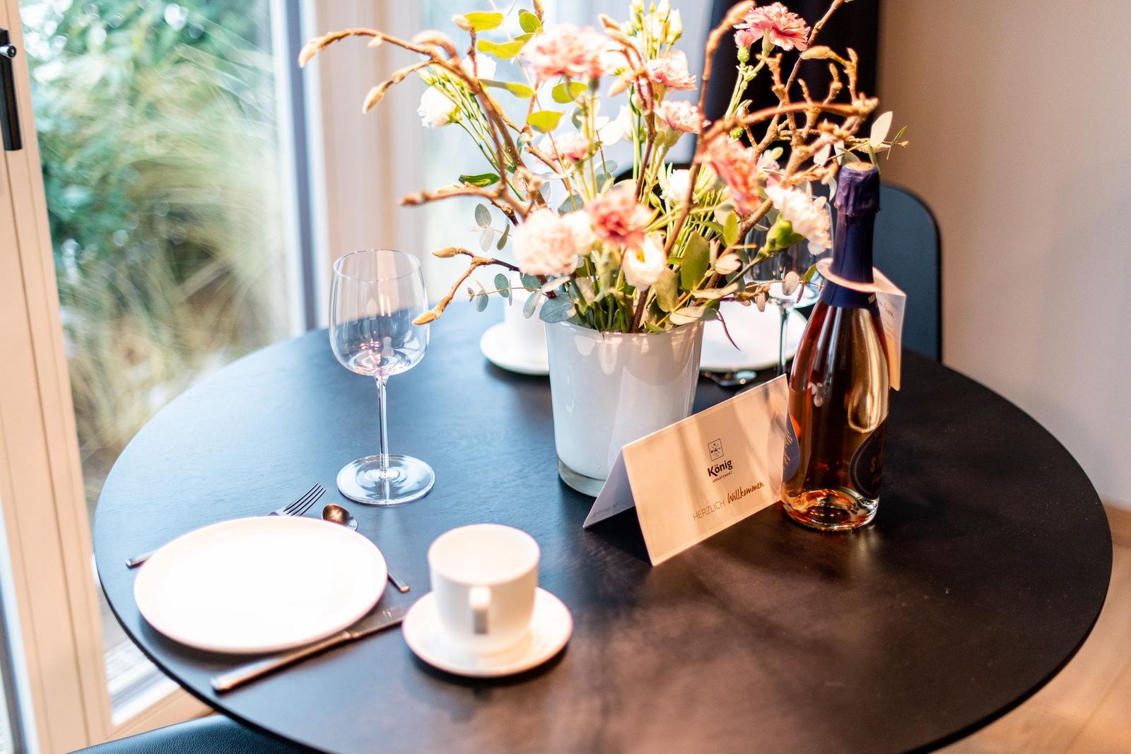 Runder Tisch mit Blumenvase, Weinflasche und Geschirr vor Fenster