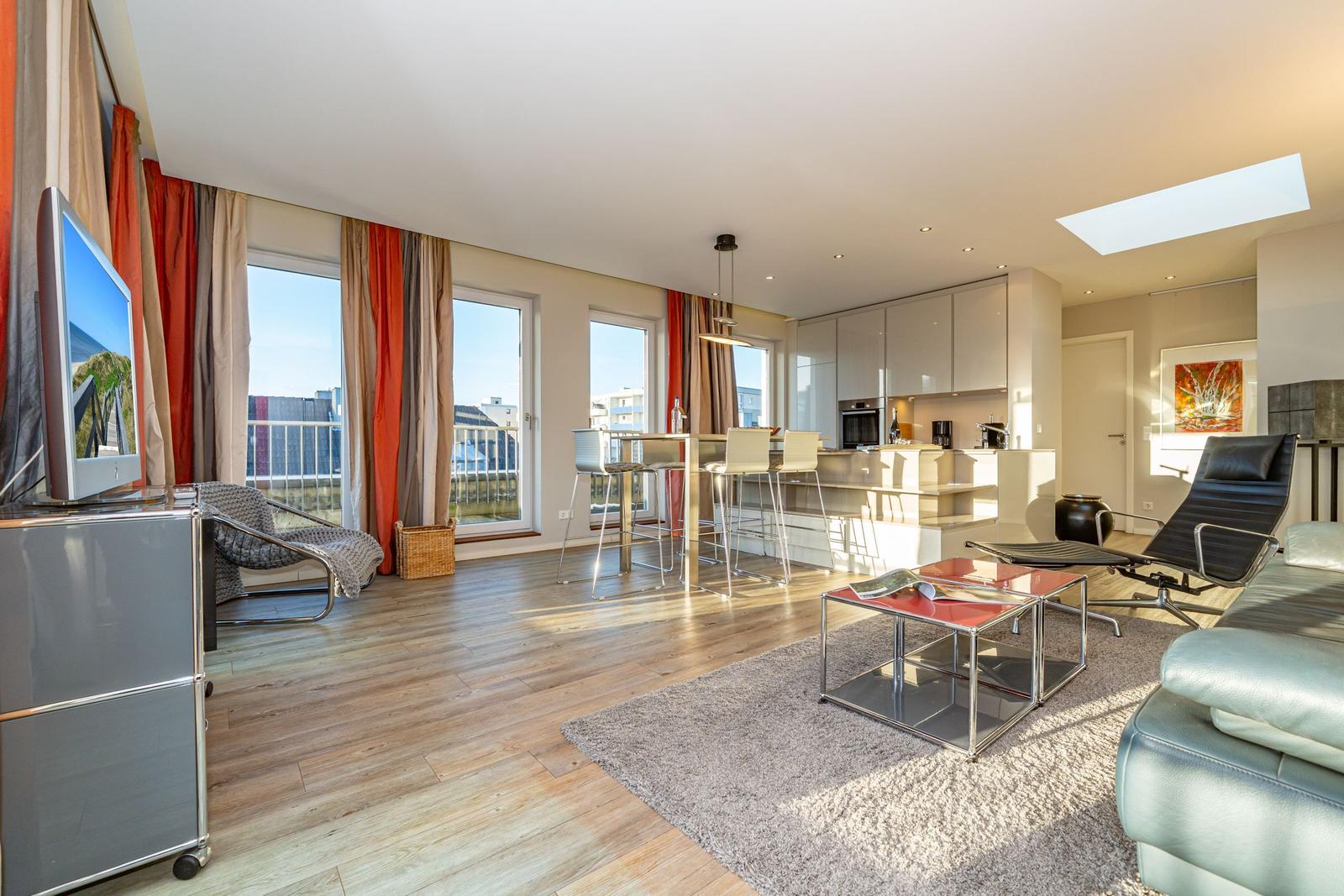 Wohnbereich mit Küchenzeile, TV, Sitzgelegenheiten und Fenster zur Aussicht.