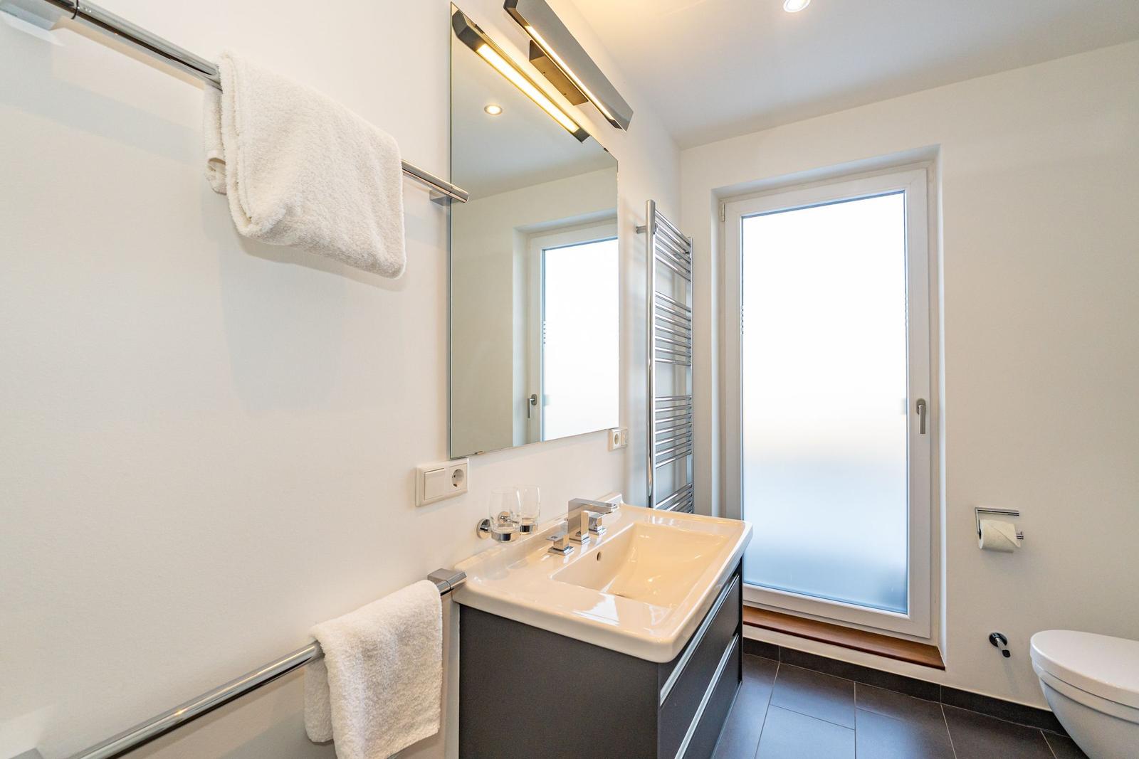 Badezimmer mit Waschbecken, Spiegel, Toilette und Dusche.