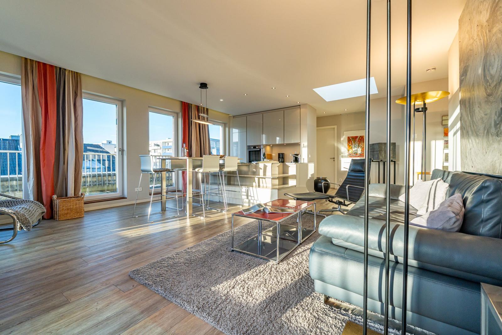 Wohn- und Essbereich mit moderner Einrichtung und großem Fenster. Küche ist offen integriert.