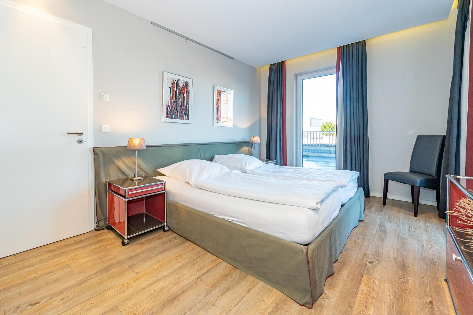 Schlafzimmer mit Doppelbett, Fenster, Stuhl und Nachttisch.