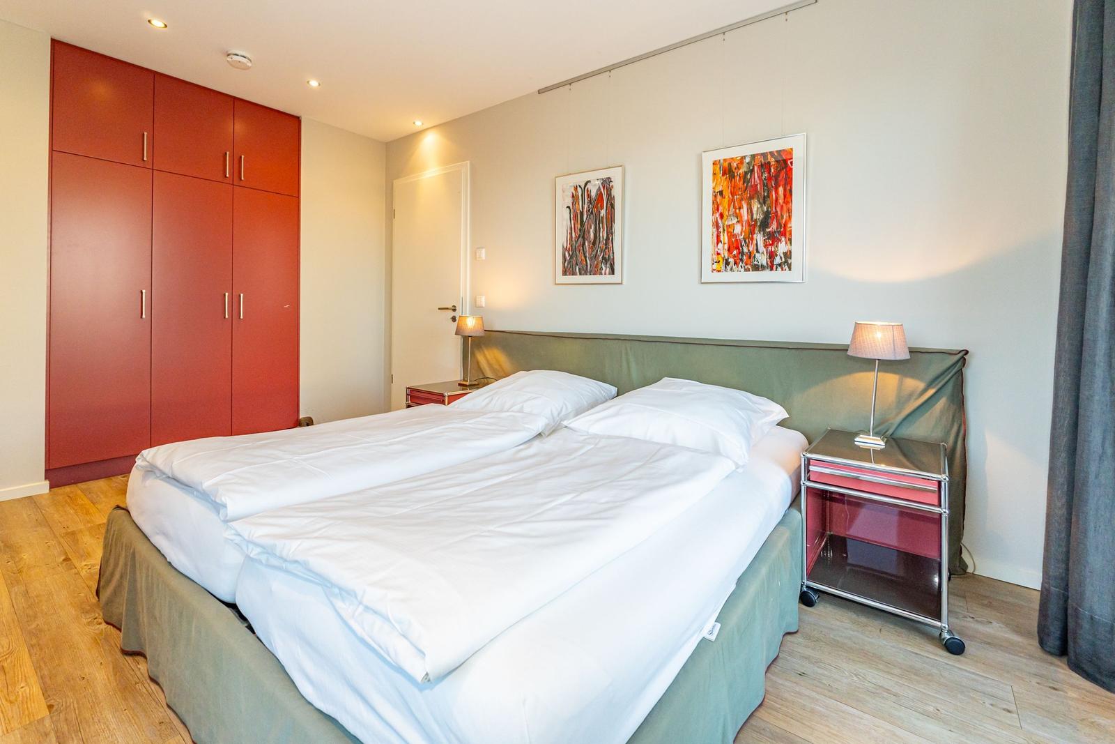 Schlafzimmer mit Doppelbett, rotem Schrank und Nachttischen mit Lampen.